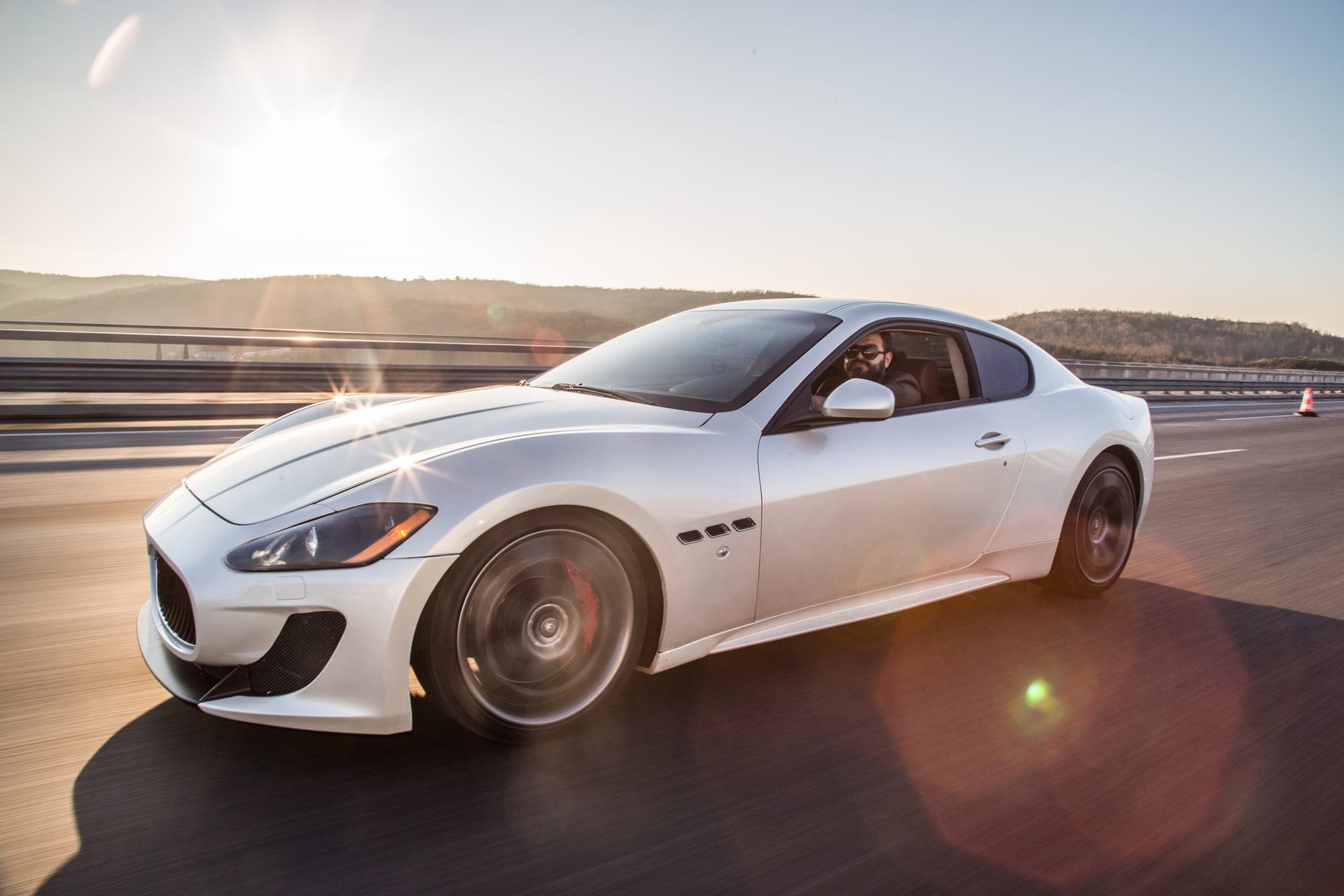 Maserati GranTurismo blanche sur une route au soleil couchant