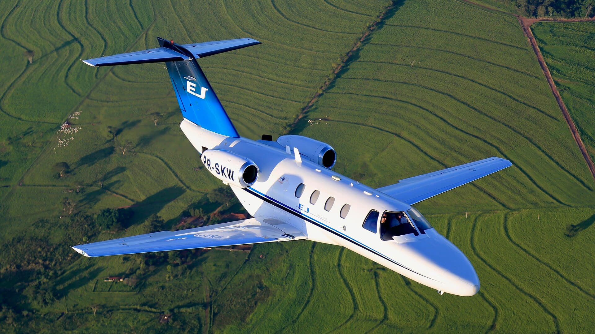 Jet privé Cessna Citation en vol au-dessus de champs verts